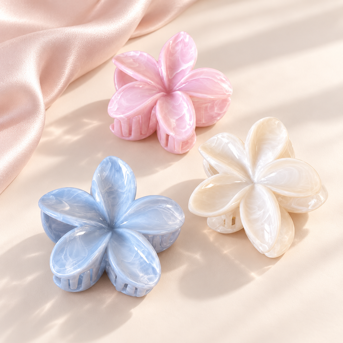 Coconoir Beauty flower hair claw clips in blue, white, and pink on an ivory surface with blush satin.