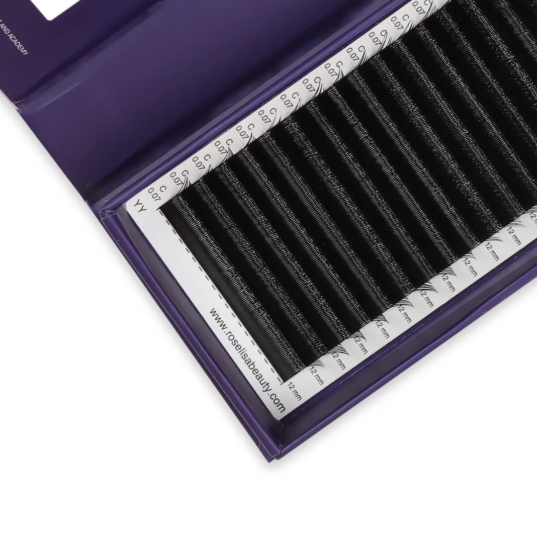A close-up of a purple lash tray containing multiple black eyelash extension tubes arranged in parallel rows, with a white measurement guide visible inside the tray.