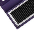 A close-up of a purple lash tray containing multiple black eyelash extension tubes arranged in parallel rows, with a white measurement guide visible inside the tray.