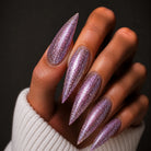 Hand with stiletto nails painted in purple glitter on a dark background