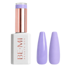 A bottle of BE-MI Beauty Box nail polish with a metallic rose gold cap and a white base, shown next to two artificial nail tips painted in a light lavender purple shade, on a neutral gray background.