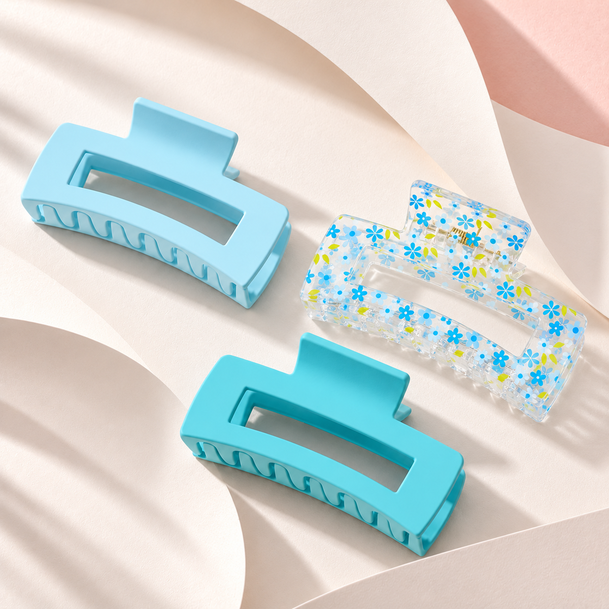 Coconoir Beauty Medium hair claw clips in Light Blue, Flowers, and Teal Blue resting on soft ivory folded paper